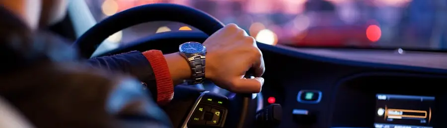 A driver's hands on the wheel at dusk, city lights ahead