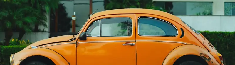 A sun-faded orange Beetle parked at the curb