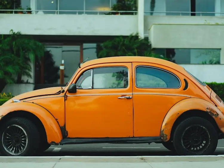 A sun-faded orange Beetle parked at the curb